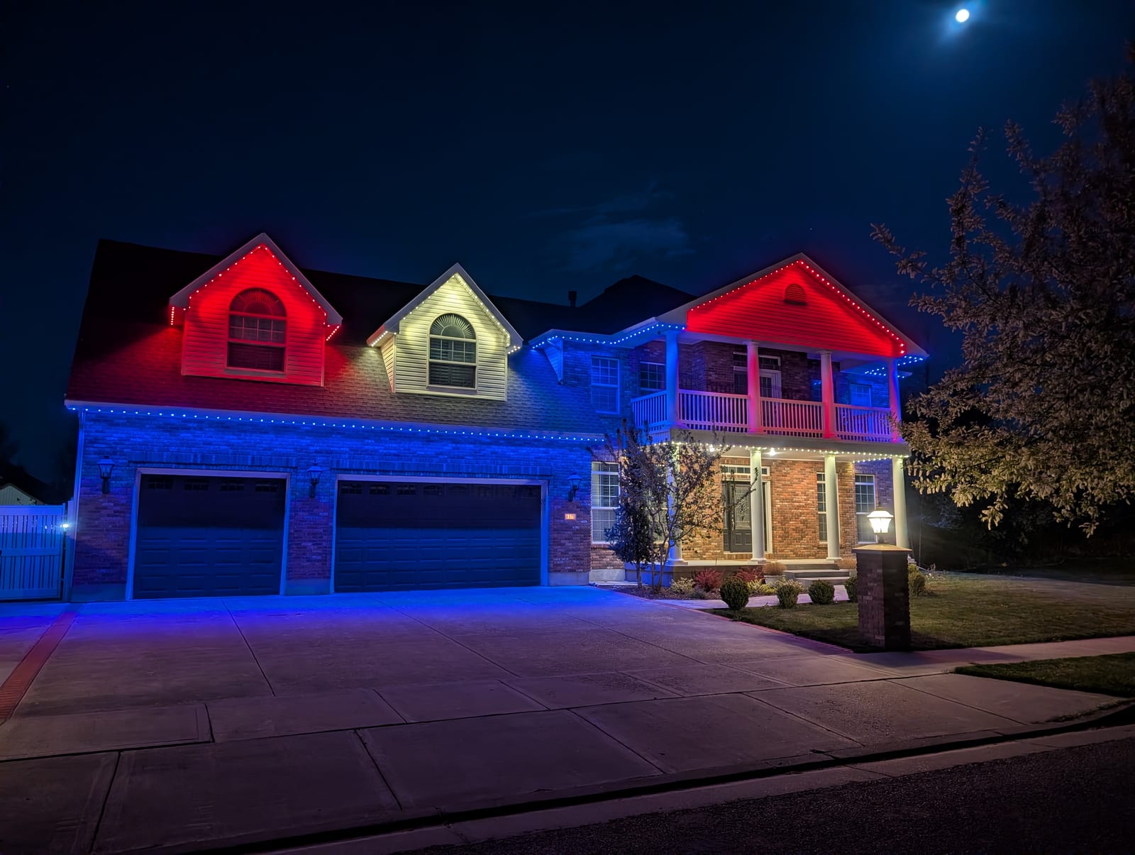 Two-story home with red, white, and blue zone-controlled permanent LED lighting across each gable and side