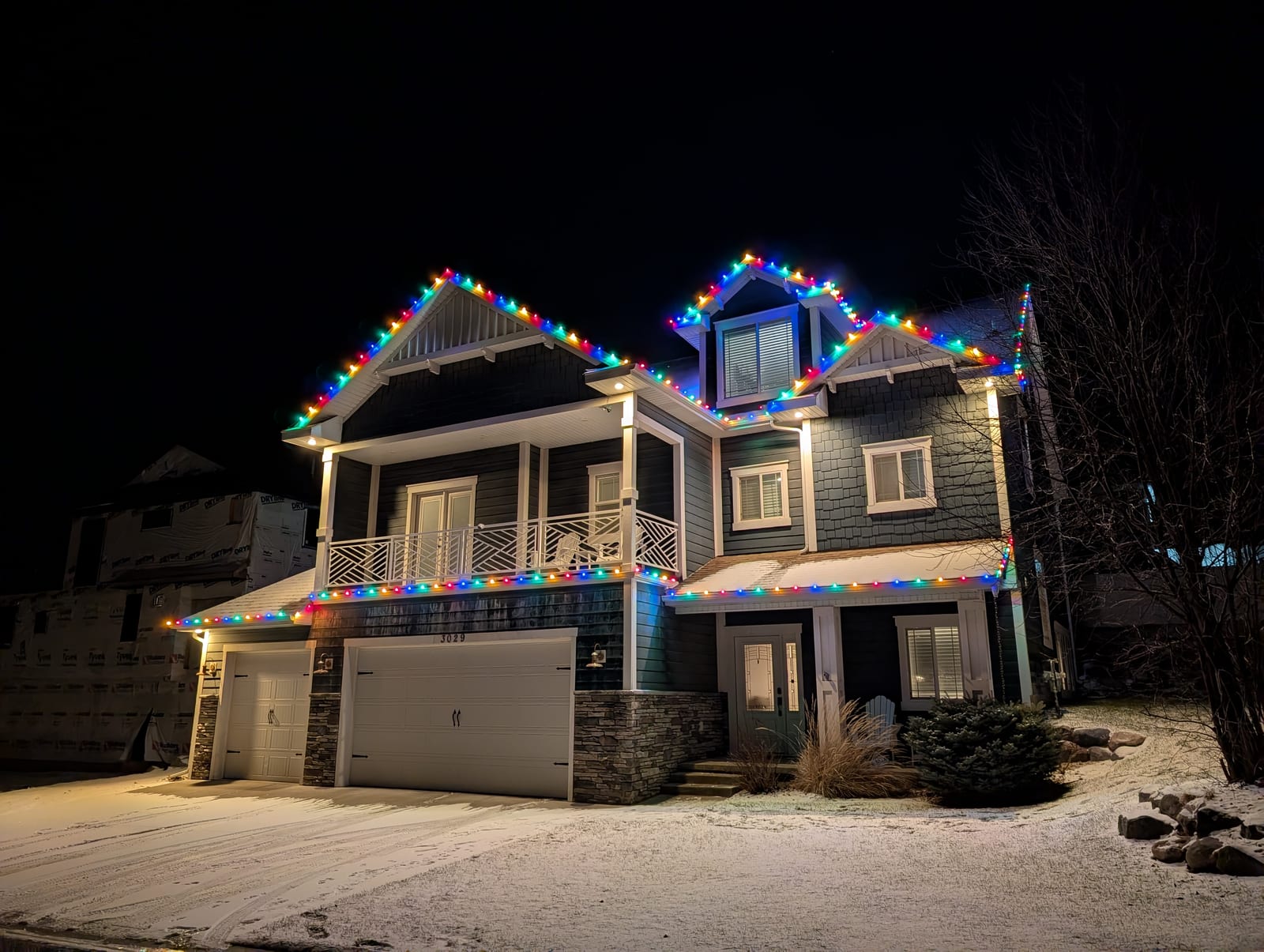Multicolor traditional Christmas lights on large two-story craftsman home in snow