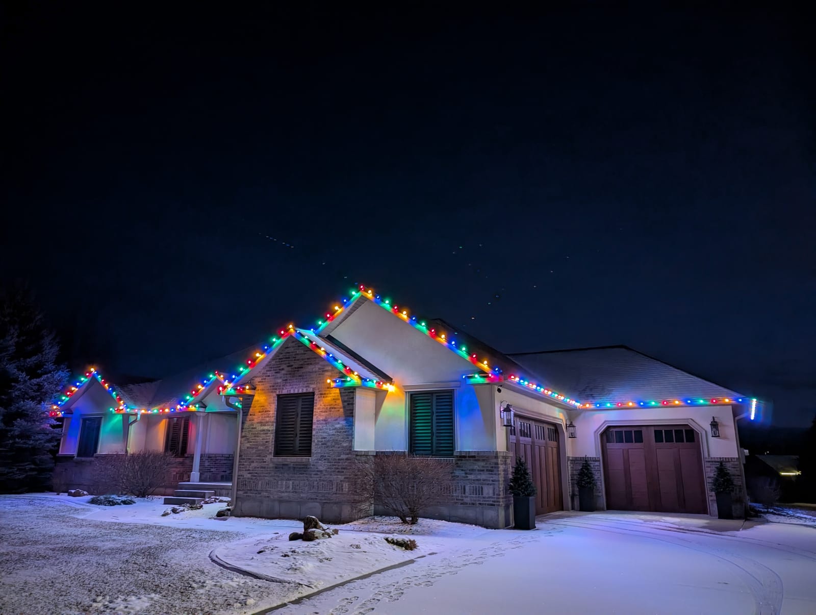 Multicolor traditional Christmas lights on ranch home roofline in fresh snow