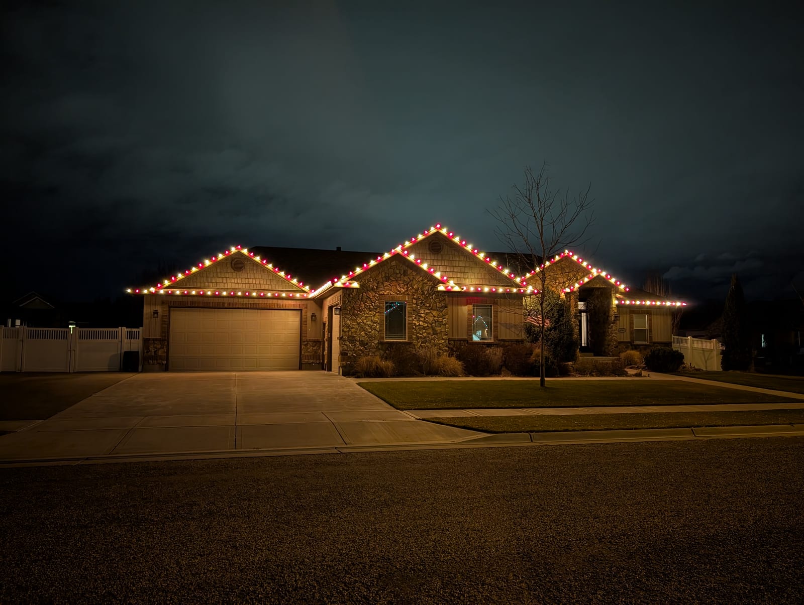 Red and gold traditional Christmas lights professionally installed on stone home roofline at dusk