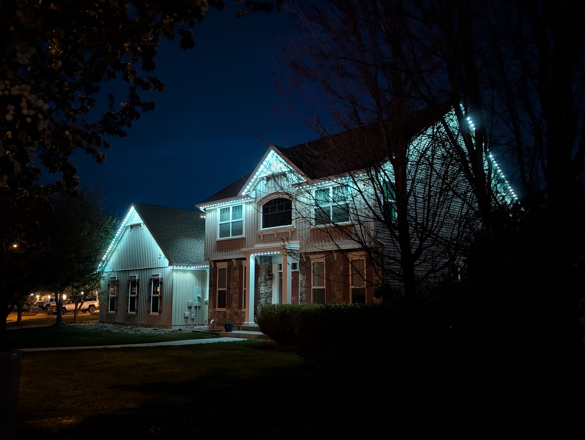 Teal smart LED exterior trim lights on two-story home - year-round permanent roofline lighting